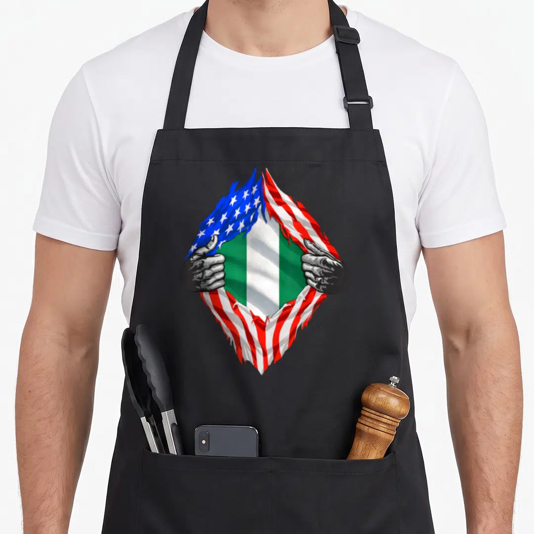 Nigeria nigerian american flag apron - Two hands tearing USA flag to reveal green white green Nigerian flag stripes — shown on a black cotton canvas apron against a white background