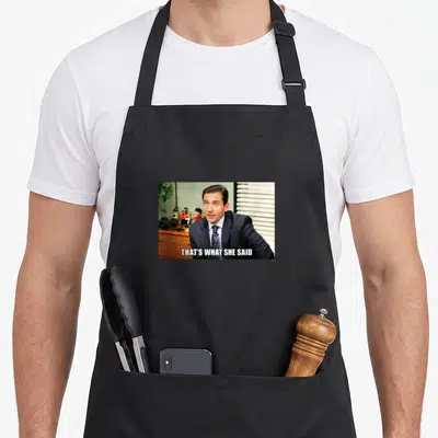 Meme michaels apron - Man in suit with white text block reading THAT'S WHAT SHE SAID across bottom — shown on a black cotton canvas apron against a white background