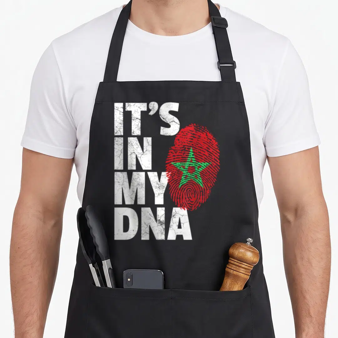 Dna moroccan apron - IT'S IN MY DNA text beside red fingerprint with green star — shown on a black cotton canvas apron against a white background