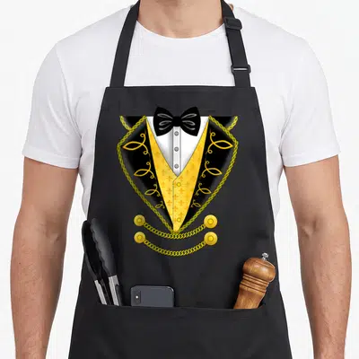 Costume circus apron - Cartoon tuxedo with yellow fleur-de-lis vest, black bow tie, and gold chains — shown on a black cotton canvas apron against a white background