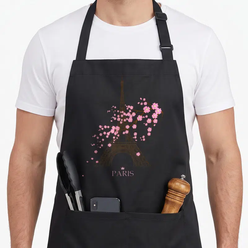 Sign paris apron - Brown Eiffel Tower line art with pink cherry blossoms and PARIS text under a crown — shown on a black cotton canvas apron against a white background