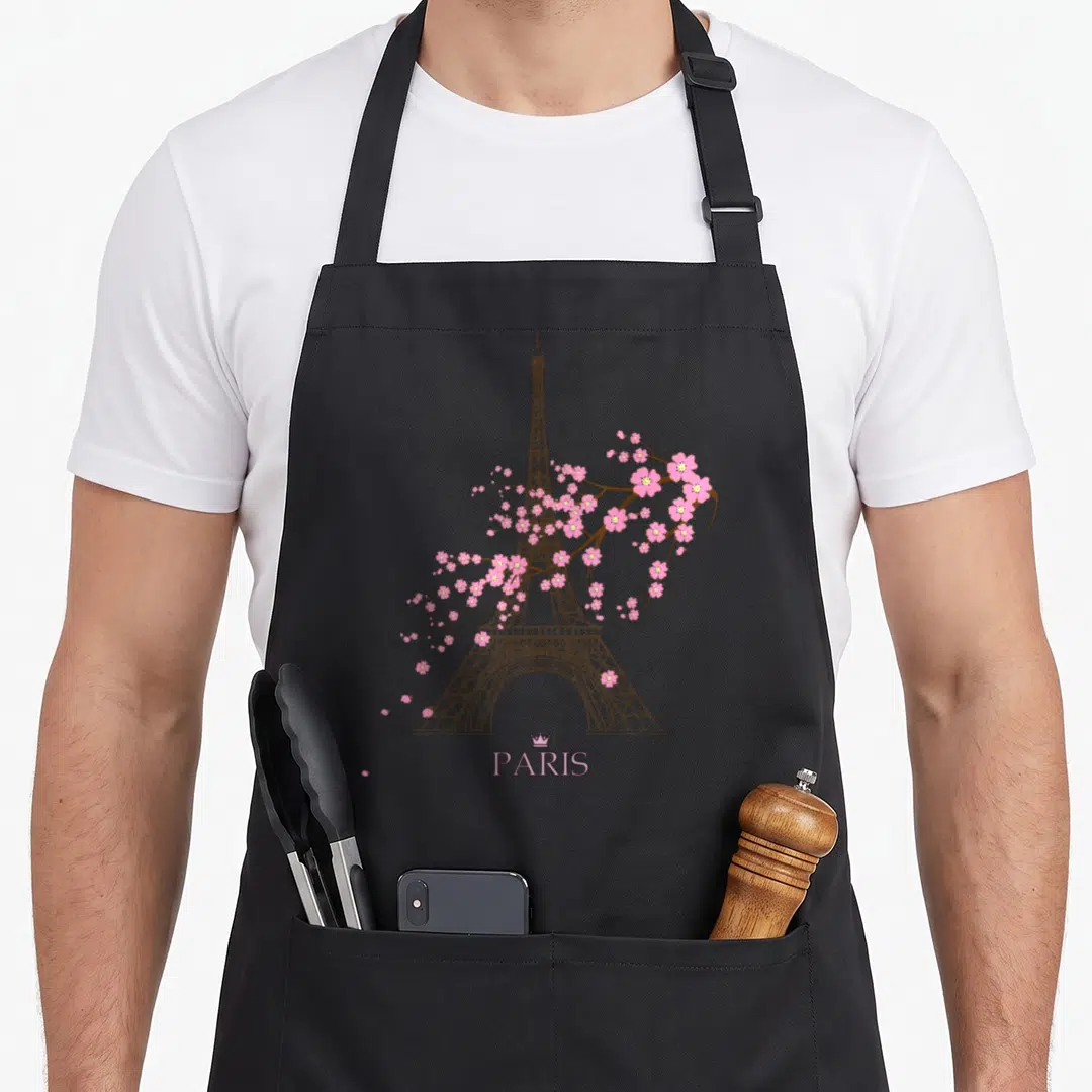 Sign paris apron - Brown Eiffel Tower line art with pink cherry blossoms and PARIS text under a crown — shown on a black cotton canvas apron against a white background