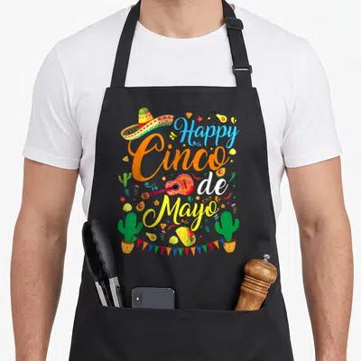 Cute cinco mexican apron - Happy Cinco de Mayo text with sombrero, guitar, cacti, and bunting flags in orange yellow — shown on a black cotton canvas apron against a white background