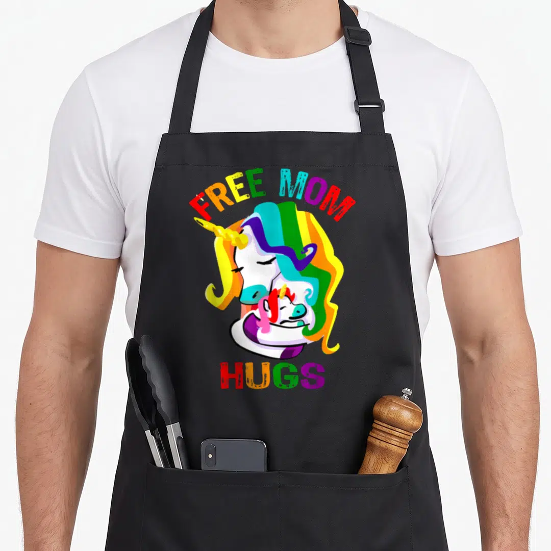 Hug lgbt gay pride apron - Free Mom Hugs text arching over two rainbow unicorns hugging in cartoon style — shown on a black cotton canvas apron against a white background