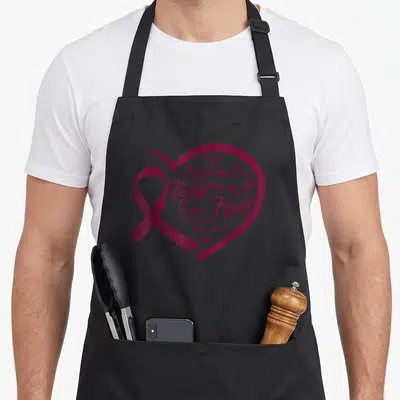 Multiple myeloma husband apron - Maroon heart outline containing awareness ribbon and text about husband's fight — shown on a black cotton canvas apron against a white background