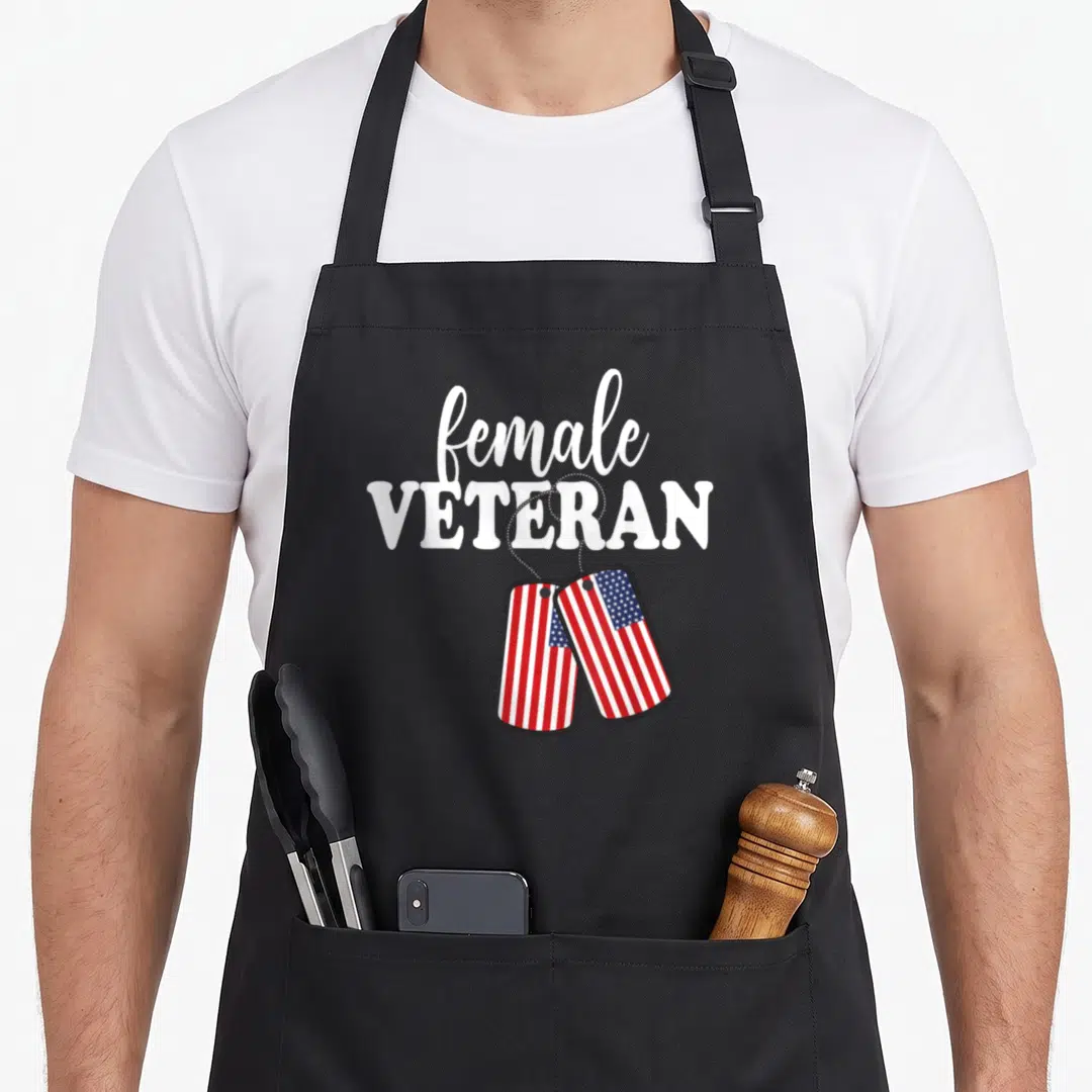 Retro female veteran apron - Female veteran text above two dog tags with red white blue flag pattern — shown on a black cotton canvas apron against a white background