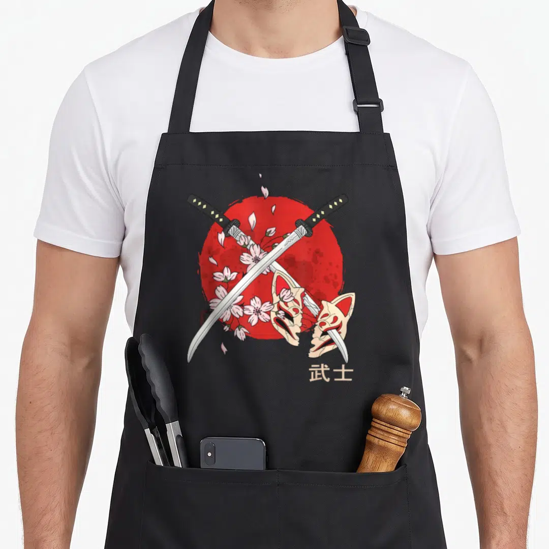 Ancient cherry print apron - Crossed silver katanas over red sun with broken beige kitsune mask and pink blossoms — shown on a black cotton canvas apron against a white background