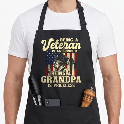 Honour patriotic apron - Distressed Uncle Sam profile with veteran grandpa text and flag background — shown on a black cotton canvas apron against a white background