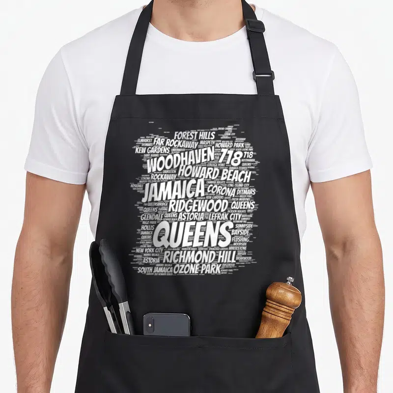 Raised new york aprons - White word cloud of Queens neighborhoods like Woodhaven, Jamaica, and Flushing forming a map — shown on a black cotton canvas apron against a white background