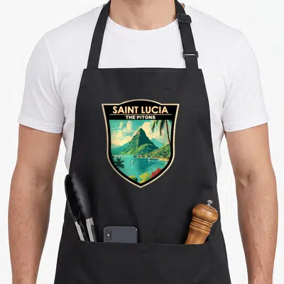 Saint travel aprons - Retro shield illustration of green Pitons mountains and teal sea with sailboats — shown on a black cotton canvas apron against a white background