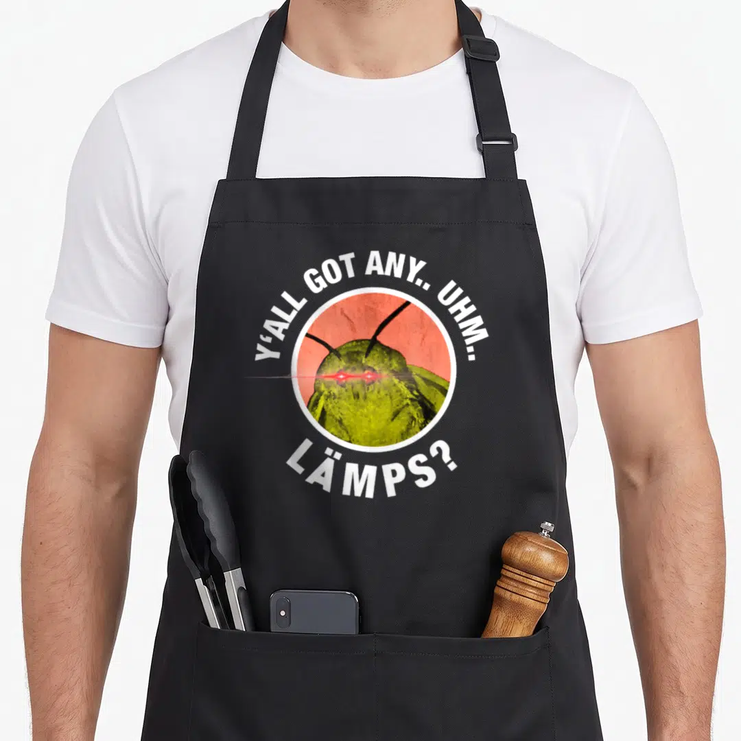 Moth meme apron - Cartoon moth with red laser eyes and Y'all Got Any Lamps text in red circle — shown on a black cotton canvas apron against a white background