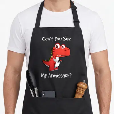 Well dinosaur apron - Red cartoon dinosaur with white arm bandage and text Can't You See My Armissaur — shown on a black cotton canvas apron against a white background