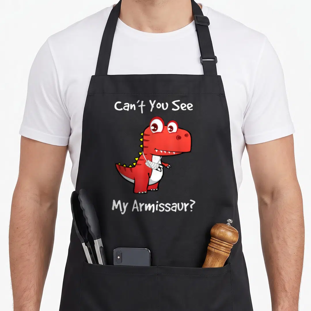 Well dinosaur apron - Red cartoon dinosaur with white arm bandage and text Can't You See My Armissaur — shown on a black cotton canvas apron against a white background