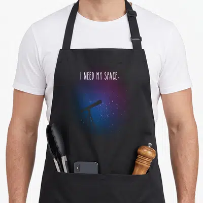 Outer nasa apron - I NEED MY SPACE text above grey telescope on tripod against purple blue starry background — shown on a black cotton canvas apron against a white background