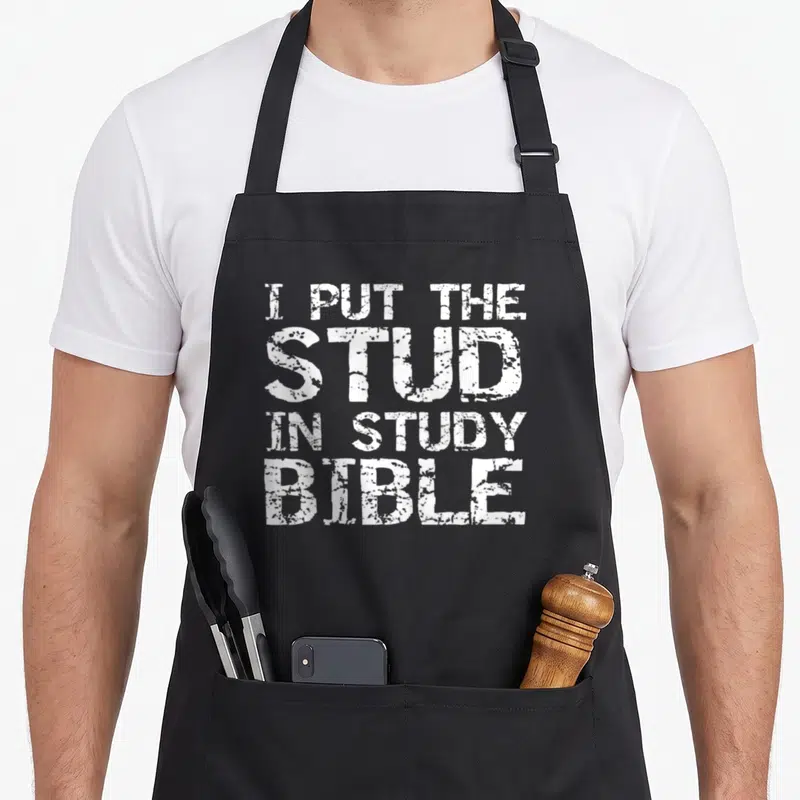 Study bible christian apron - White distressed text reading I PUT THE STUD IN STUDY BIBLE stacked in four lines — shown on a black cotton canvas apron against a white background