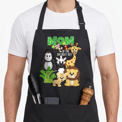 Theme animal birthday apron - Cartoon gorilla lion zebra giraffe monkey snake parrot leopard with MOM OF THE BIRTHDAY — shown on a black cotton canvas apron against a white background