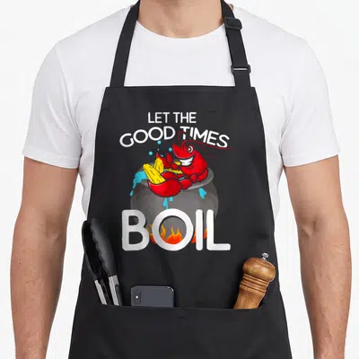 Crawdaddy crawfish boil apron - Cartoon red crawfish in grey pot with corn and text Let The Good Times Boil — shown on a black cotton canvas apron against a white background