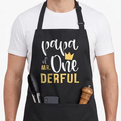 Papa birthday apron - Stacked white and yellow text reading papa of One MR. DERFUL with a small gold crown — shown on a black cotton canvas apron against a white background
