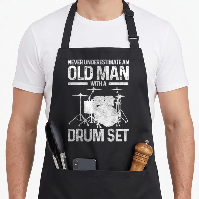 Drummer drum kit apron - White distressed text reading Never Underestimate An Old Man With A Drum Set above and below — shown on a black cotton canvas apron against a white background