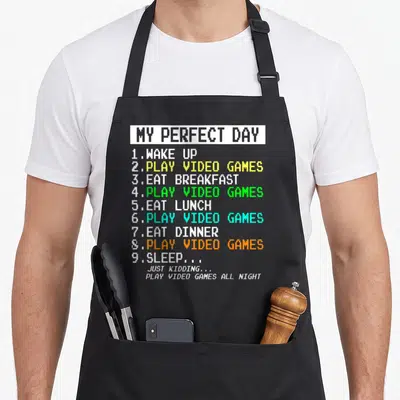 Gaming video game apron - Pixel text list My Perfect Day Play Video Games All Night — shown on a black cotton canvas apron against a white background