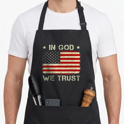 God trust american flag apron - Distressed USA flag with IN GOD WE TRUST text and two flanking stars — shown on a black cotton canvas apron against a white background