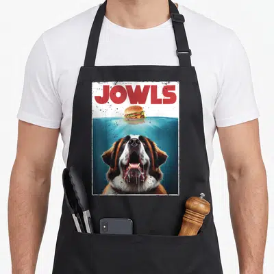 Bernard jowl dog apron - JOWLS text, floating burger, submerged Saint Bernard head with drool — shown on a black cotton canvas apron against a white background