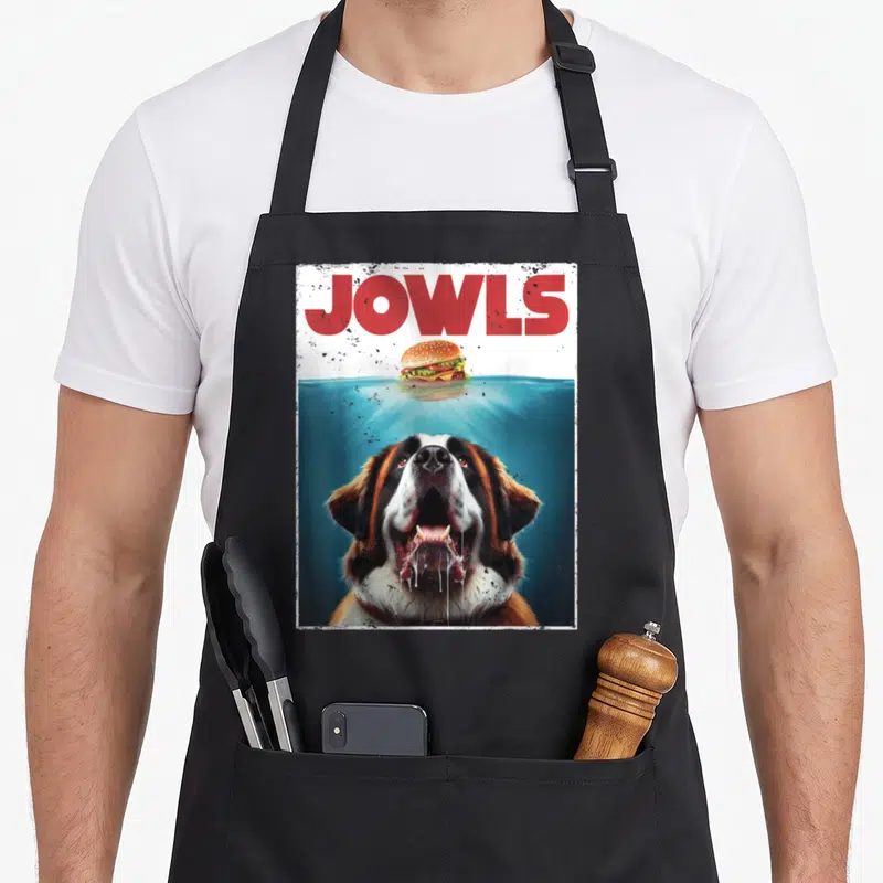 Bernard jowl dog apron - JOWLS text, floating burger, submerged Saint Bernard head with drool — shown on a black cotton canvas apron against a white background