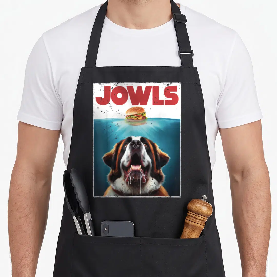 Bernard jowl dog apron - JOWLS text, floating burger, submerged Saint Bernard head with drool — shown on a black cotton canvas apron against a white background