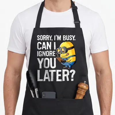 Despicable later apron - Yellow minion in blue overalls holding notebook beside white text asking to be ignored later — shown on a black cotton canvas apron against a white background