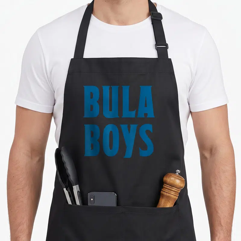 Bula fiji apron - Blue stacked text reading BULA BOYS in bold serif font — shown on a black cotton canvas apron against a white background