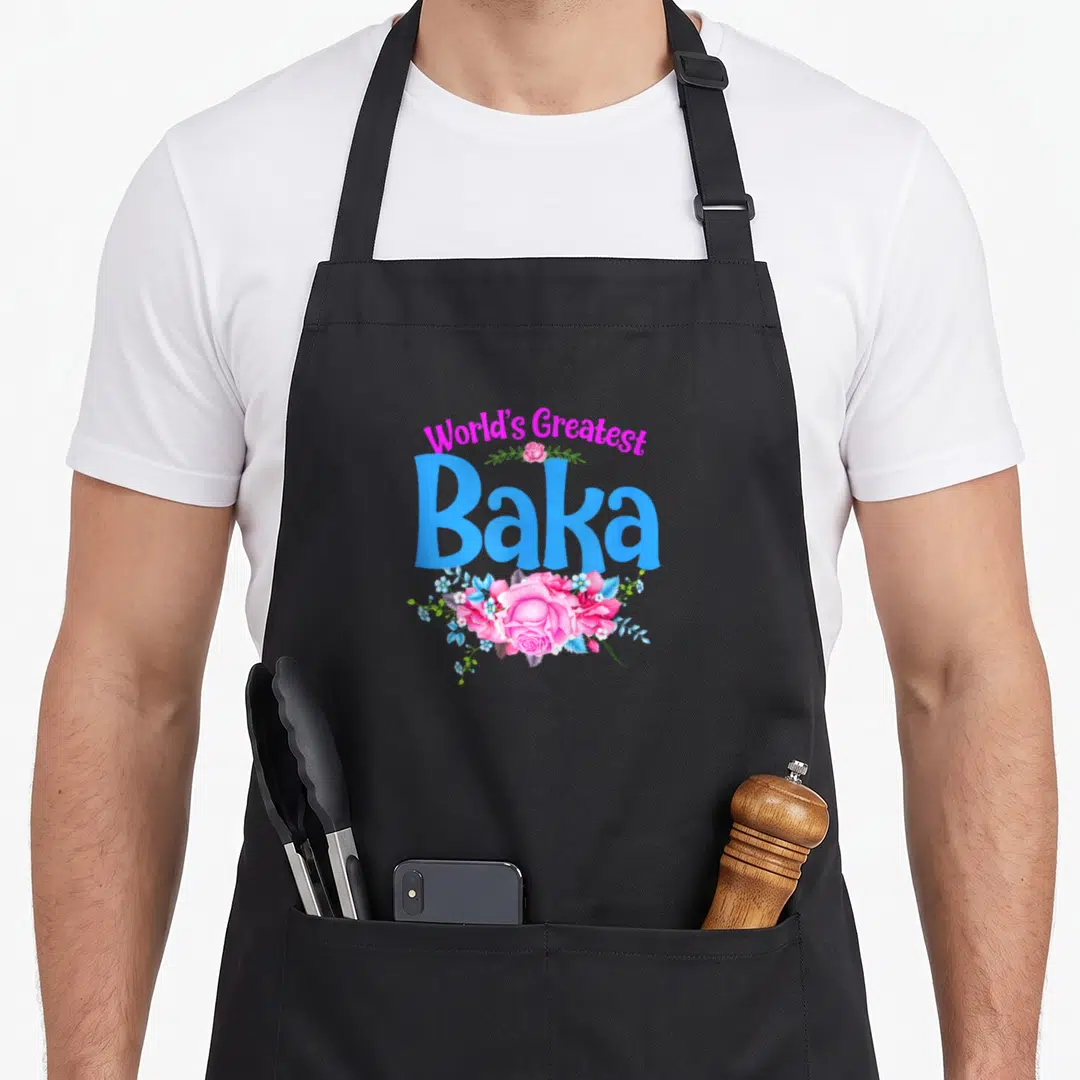Greatest croatian aprons - Arched pink text World's Greatest above blue Baka with pink and blue flower cluster — shown on a black cotton canvas apron against a white background