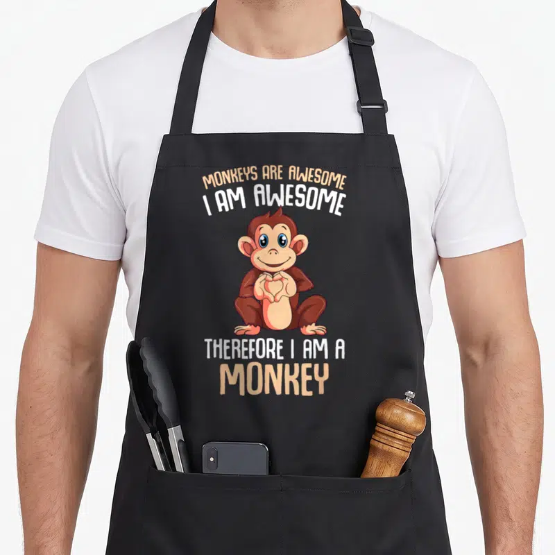 Vintage monkey apron - Cartoon monkey making heart shape with text Monkeys Are Awesome I Am Awesome Therefore I Am — shown on a black cotton canvas apron against a white background