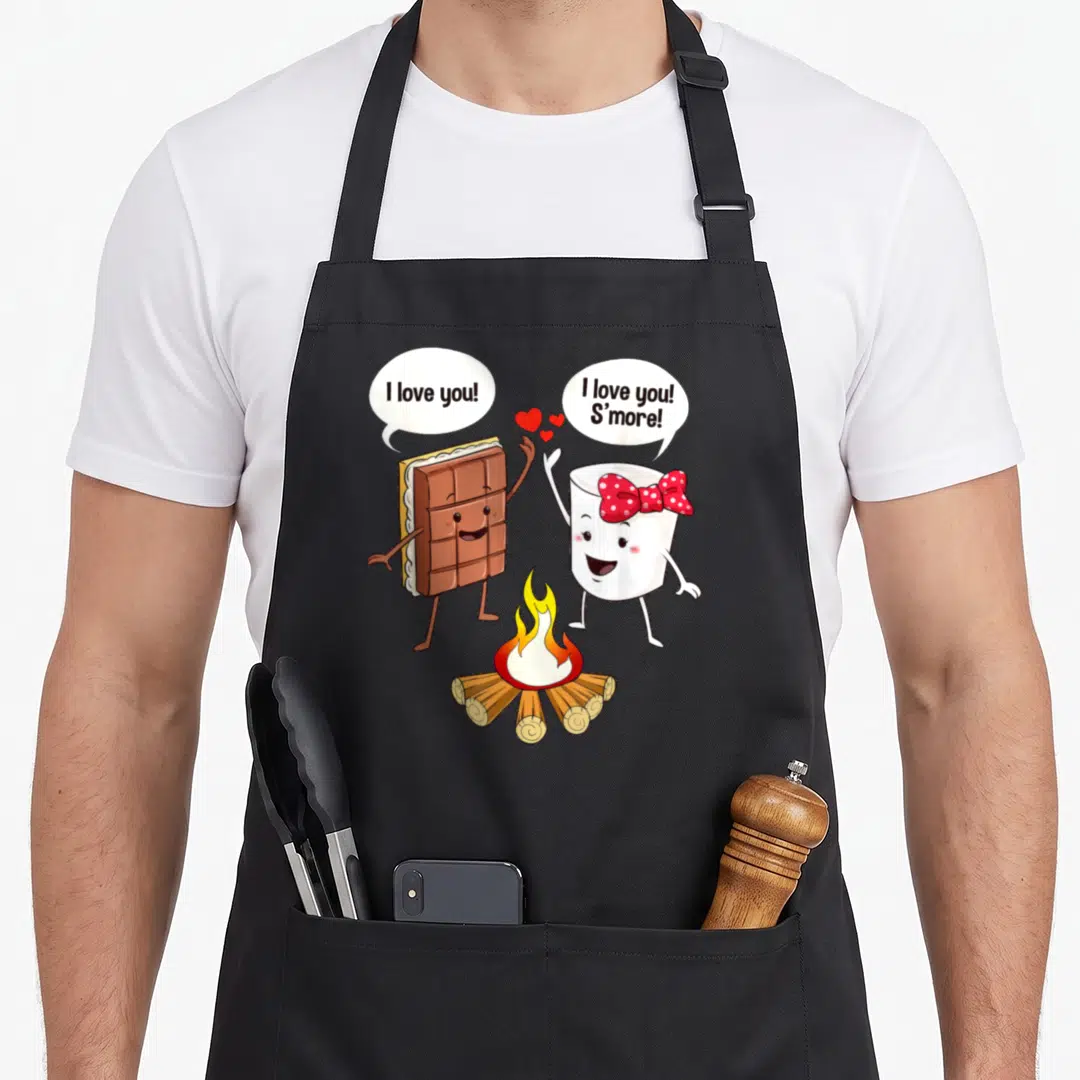 Funny smore camping apron - Cartoon s'more characters with speech bubbles over a campfire — shown on a black cotton canvas apron against a white background
