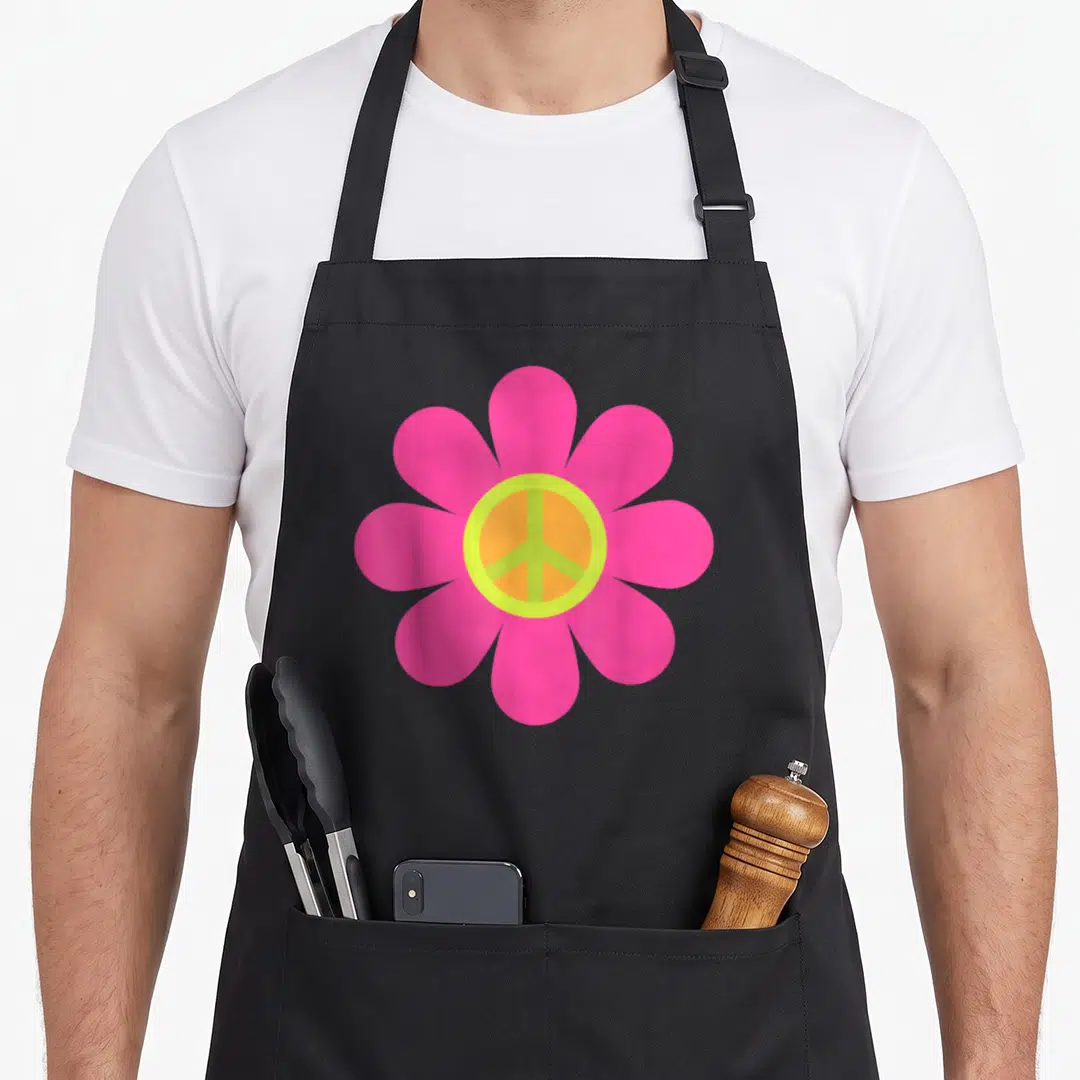 70s hippie apron - Pink flower with yellow and orange peace sign in center — shown on a black cotton canvas apron against a white background