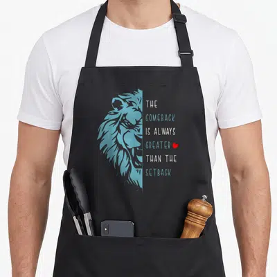 Comeback lion apron - Blue lion profile facing right next to stacked inspirational text and small red heart — shown on a black cotton canvas apron against a white background