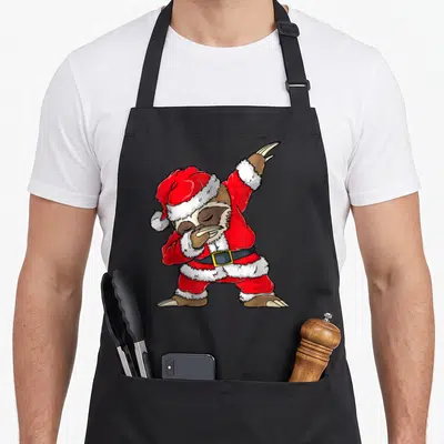 Sloth merry christmas apron - Cartoon sloth in red Santa suit dabbing with brown claws and black belt — shown on a black cotton canvas apron against a white background