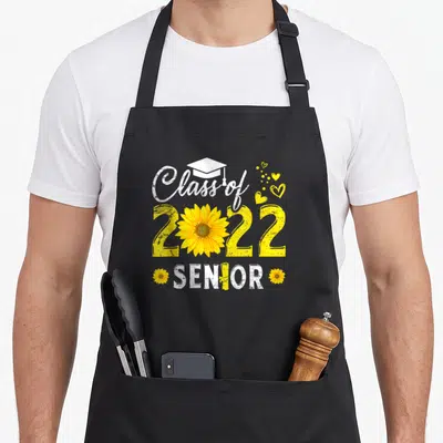 Graduation sunflower apron - Class of 2022 SENIOR text with yellow sunflower and white cap graphic — shown on a black cotton canvas apron against a white background