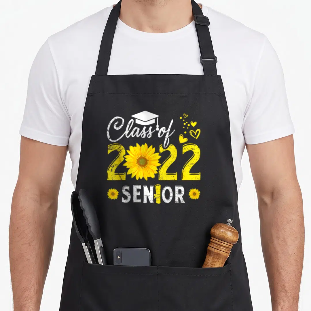Graduation sunflower apron - Class of 2022 SENIOR text with yellow sunflower and white cap graphic — shown on a black cotton canvas apron against a white background