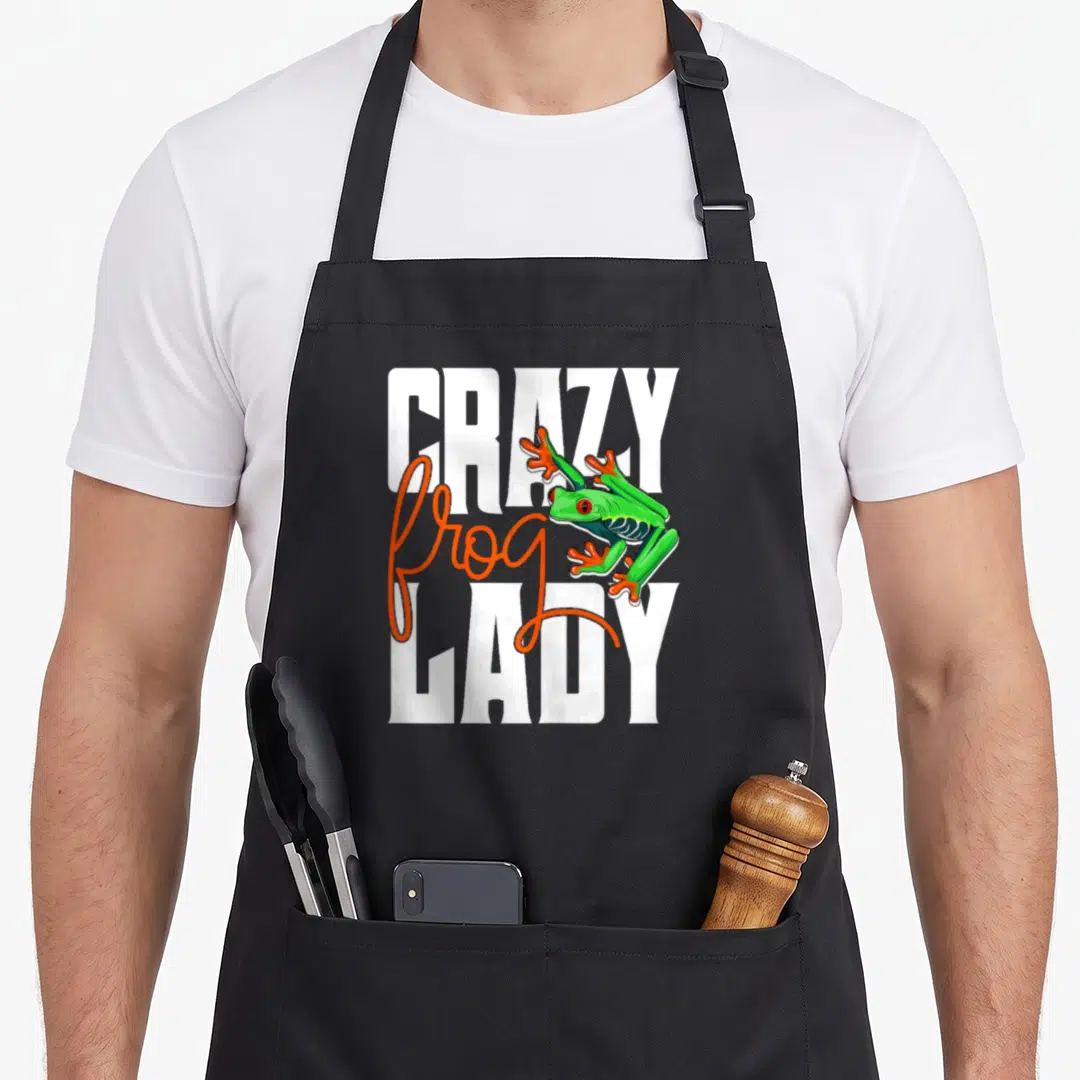 Amphibian owner frog aprons - Green frog with orange feet perched over white and orange CRAZY LADY text — shown on a black cotton canvas apron against a white background
