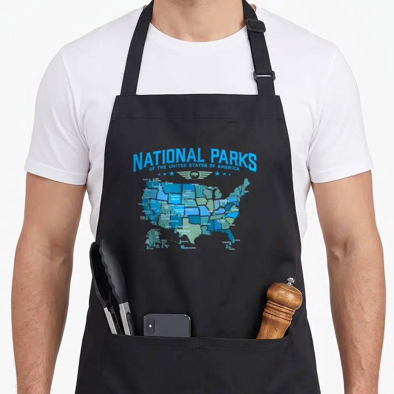 80s camping apron - Blue map of USA with National Parks text, bison, stars, and small trees in minimalist style — shown on a black cotton canvas apron against a white background