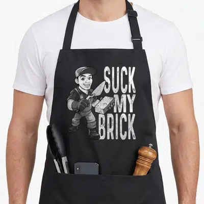 Hard mason apron - Cartoon mason holding trowel and brick next to stacked white text Suck My Brick on grey background — shown on a black cotton canvas apron against a white background