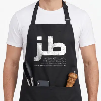 Toz sarcastic apron - White Arabic calligraphy and explanatory text block on dark background — shown on a black cotton canvas apron against a white background