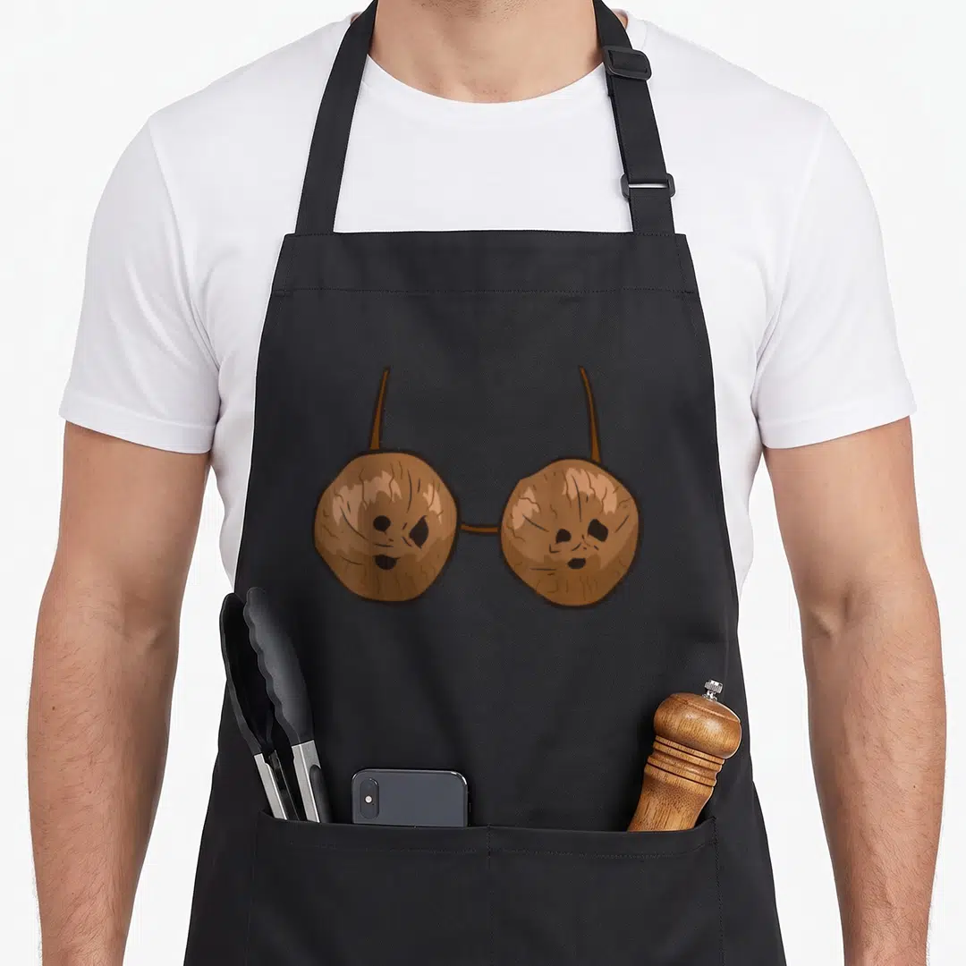 Coconut summer aprons - Two brown cartoon coconut halves connected by straps resembling a bikini top — shown on a black cotton canvas apron against a white background