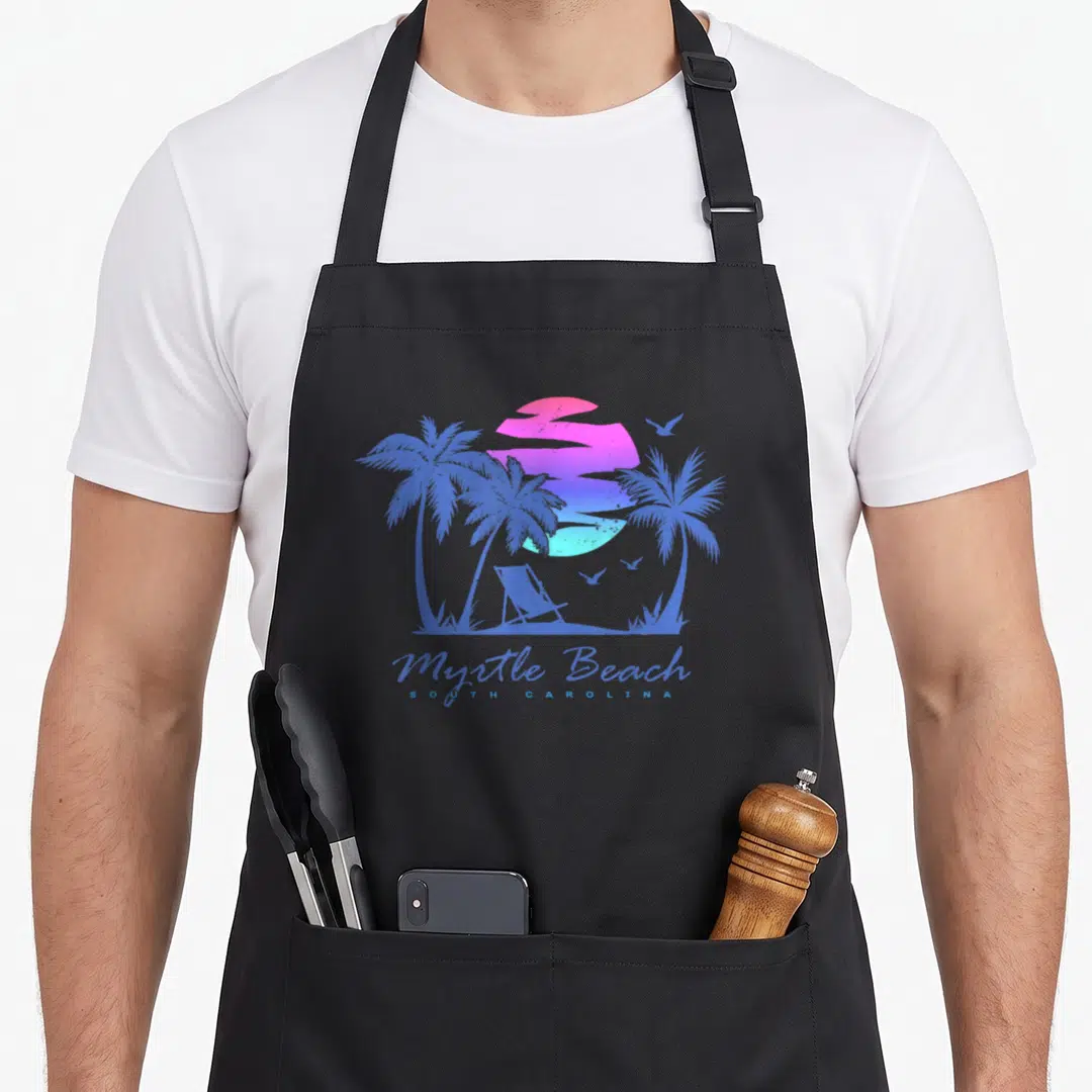 Vacation myrtle beach apron - Retro blue and pink sunset with palm trees, beach chair, and Myrtle Beach South Carolina — shown on a black cotton canvas apron against a white background