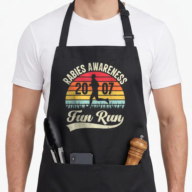 Raby comedy apron - Rabies Awareness 2007 Fun Run retro striped sun runner silhouette — shown on a black cotton canvas apron against a white background