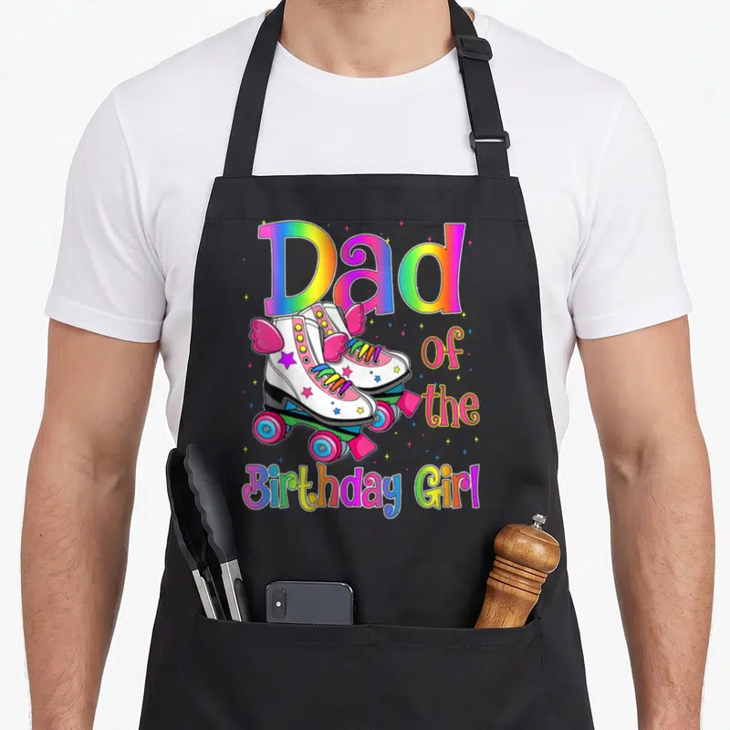 Rolling family cooking aprons - Rainbow Dad of Birthday Girl text with two winged white roller skates and colorful stars — shown on a black cotton canvas apron against a white background