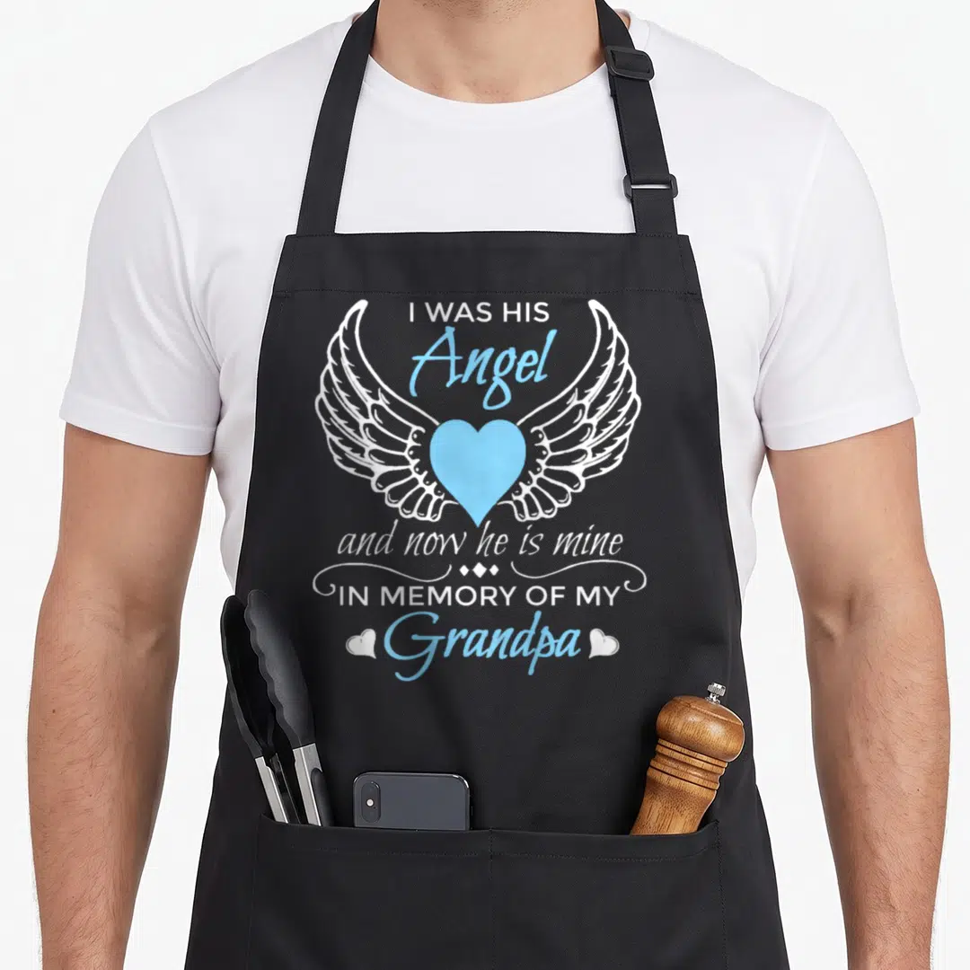 Grandpa angels and aprons - White wings flanking a blue heart with memorial text for Grandpa — shown on a black cotton canvas apron against a white background