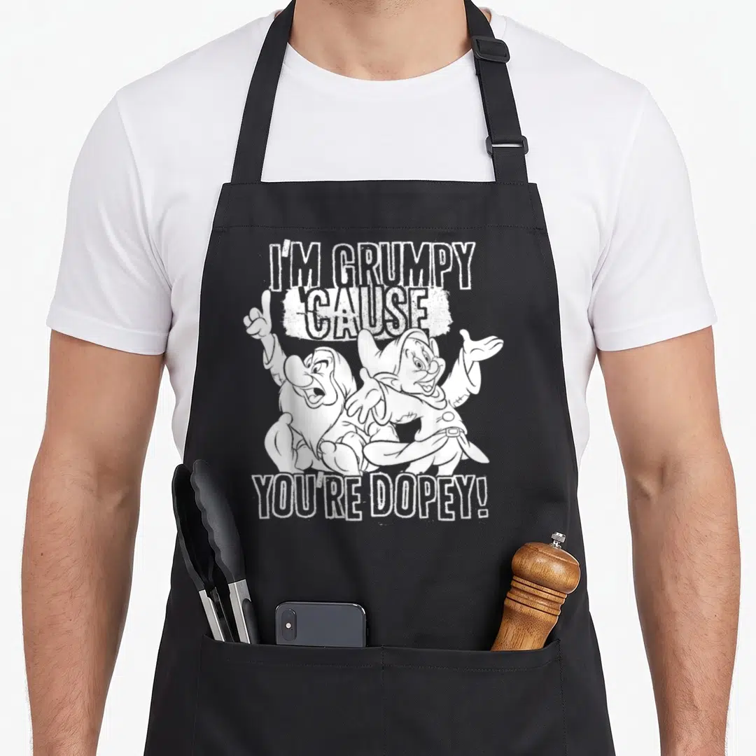 Cause snow white apron - White cartoon line art of two dwarves with text I'm Grumpy Cause You're Dopey on black fabric — shown on a black cotton canvas apron against a white background