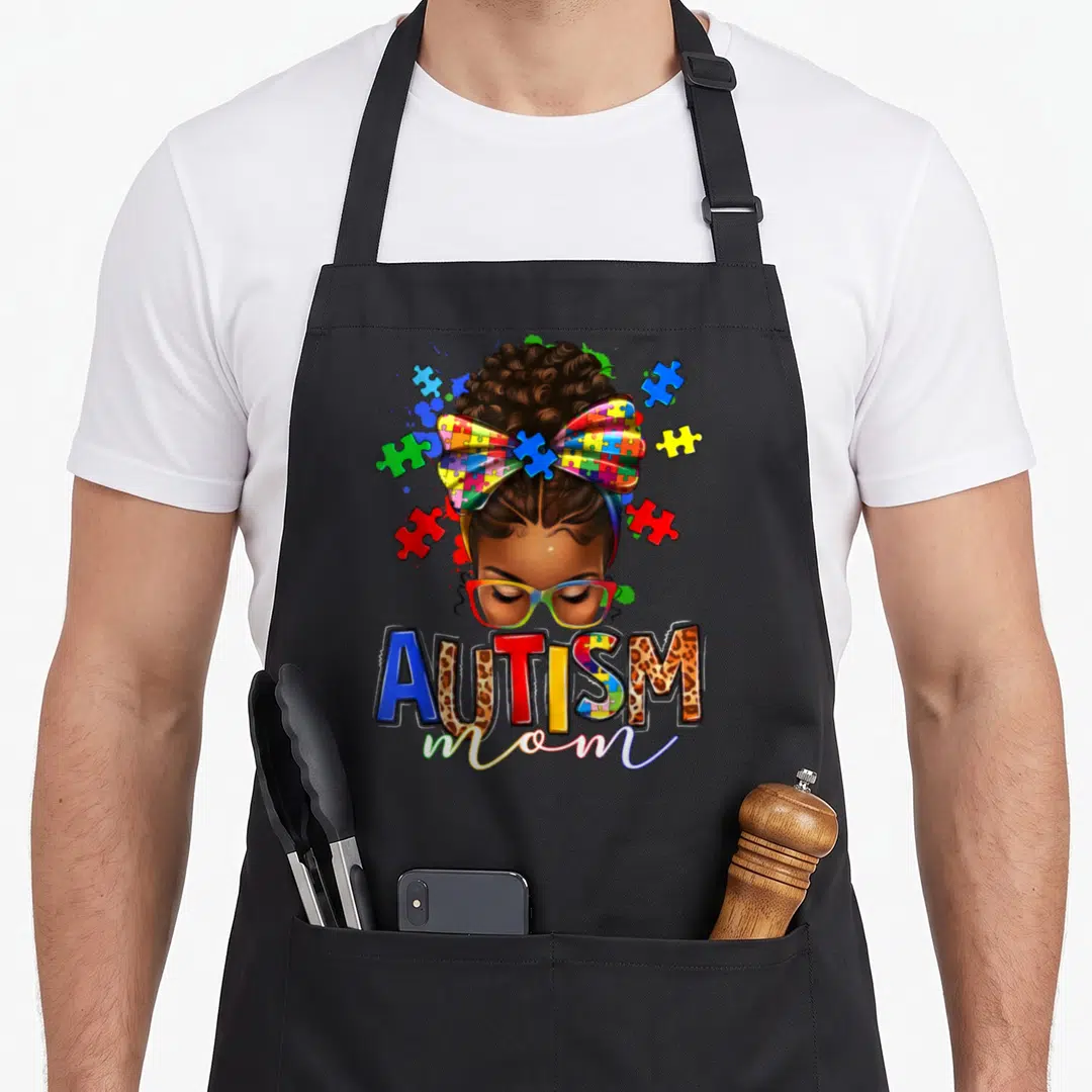 Awareness messy aprons - Cartoon woman with rainbow glasses and puzzle bow with AUTISM mom text — shown on a black cotton canvas apron against a white background