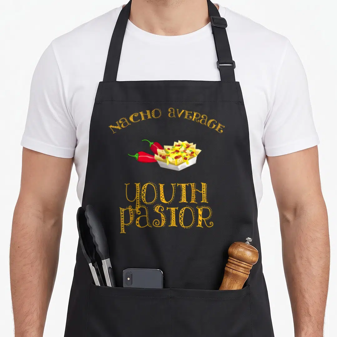 Pastor mexican apron - Cartoon nachos in a bowl with two peppers and nacho average youth pastor text — shown on a black cotton canvas apron against a white background